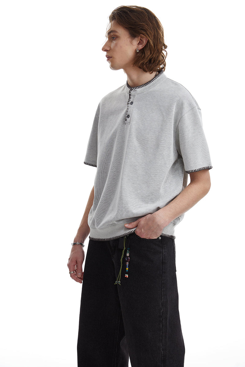 Light gray relaxed-fit Henley tee with contrast stitching, short sleeves, and button placket on a male model