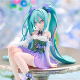 The Hatsune Miku Fairy 13.5cm PVC Figure, with long teal twin-tails and a fairy-inspired design, features a white, purple, and green outfit with floral accents. She sits gracefully on a reflective surface against a blurred pastel background, perfect for display.