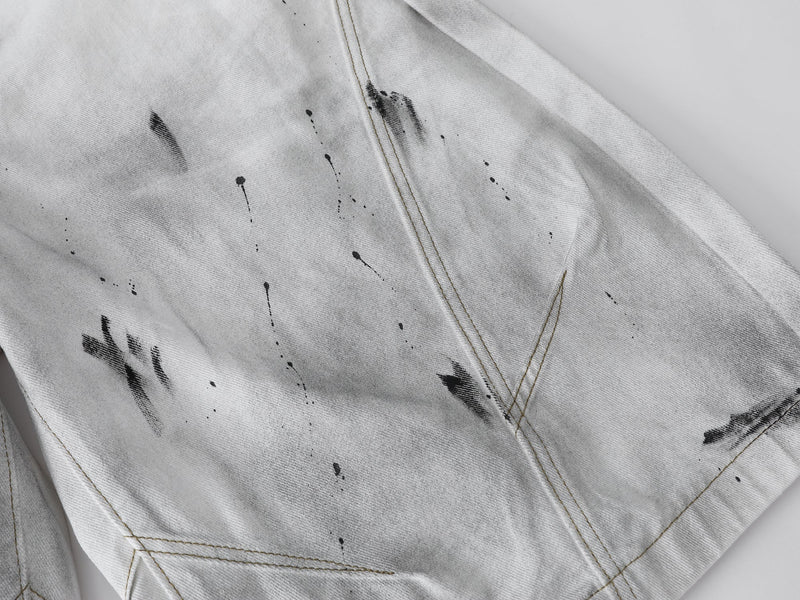 Close-up of the leg panel on white denim shorts with black splatter and seam stitching