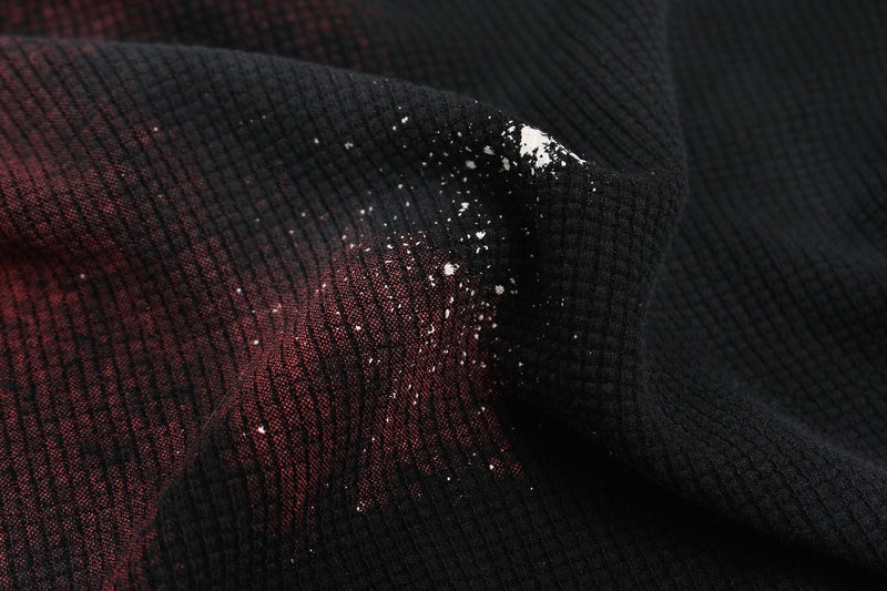 Close-up of black washed oversized tee fabric with faded red shadow figure print and distressed speckled detail