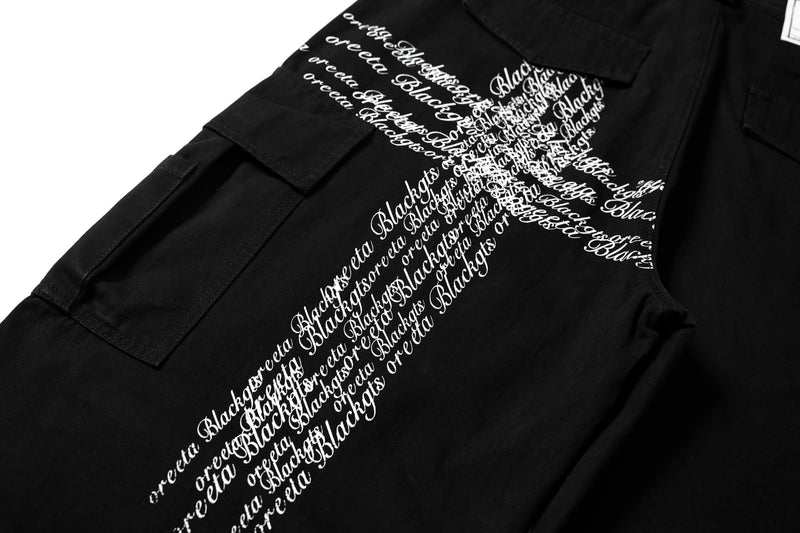 Close-up of side cargo pocket and large white cross script graphic on black pants