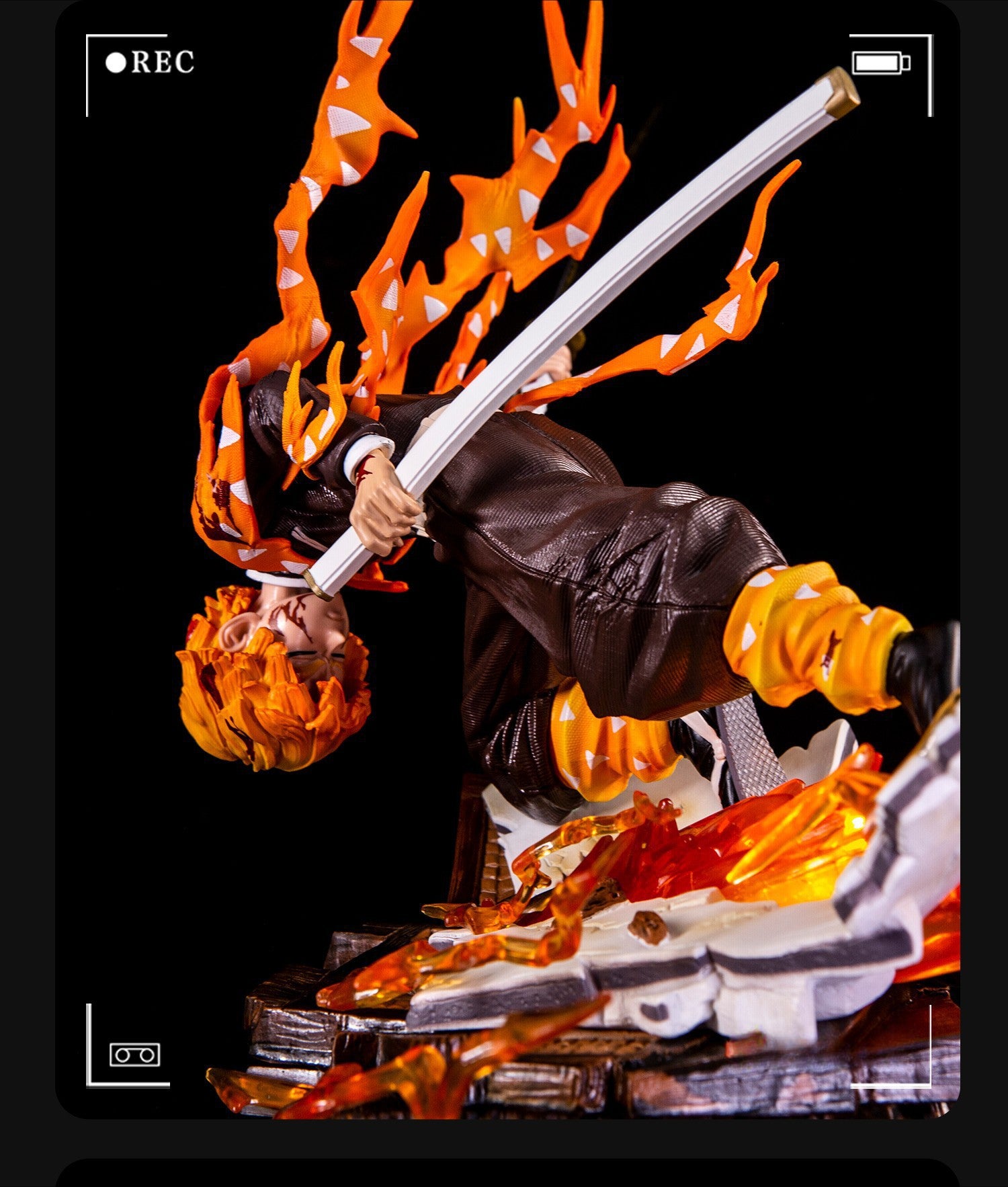 The Rengoku Kyojuro Demon Slayer Figure - Flame Hashira - 28cm is a dynamic PVC piece by Demon Slayer, featuring the character with yellow spiky hair in a fiery cloak, posed mid-air wielding a large sword. The base has flame and debris details, with an image &quot;REC&quot; frame for a camcorder effect.