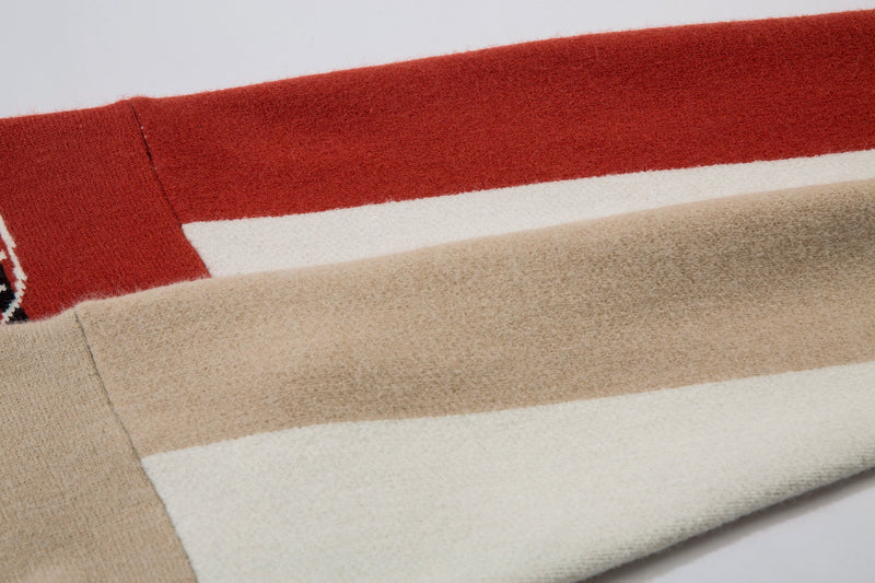 Close-up of beige sleeve, cream stripe, and red shoulder on cable-knit jacket