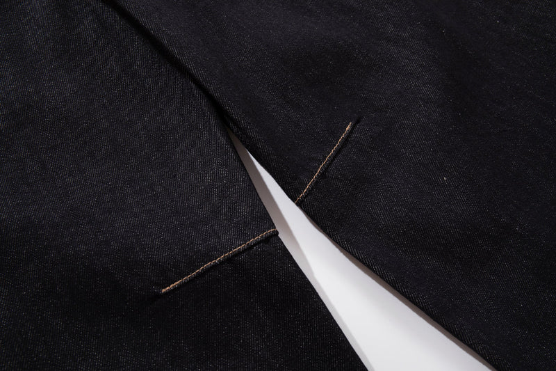 Close-up of dark wash denim pant legs with tan stitched seam detail