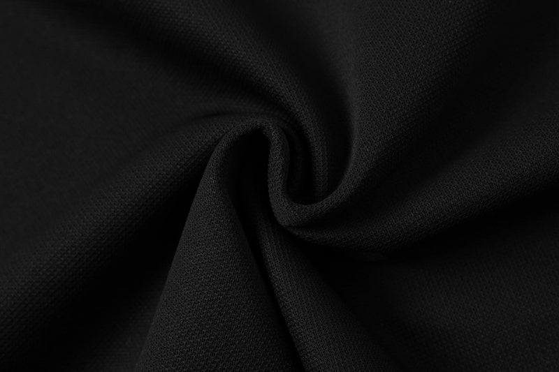 Close-up of black textured polo fabric with a subtle mesh weave and soft folded drape