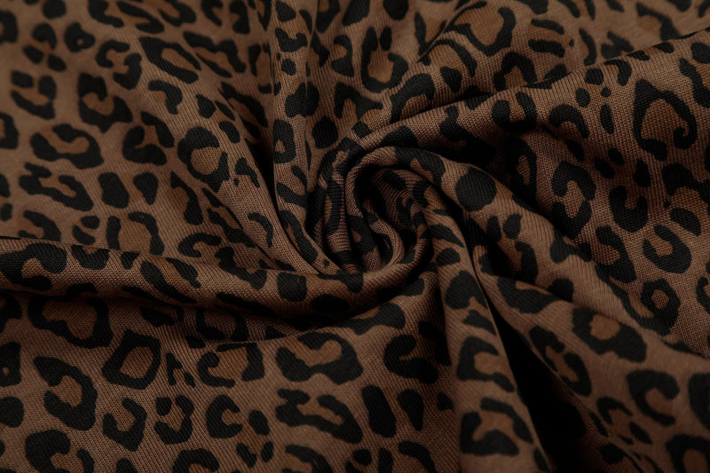Close-up of brown leopard print polo tee fabric with black script-style pattern and soft folded texture