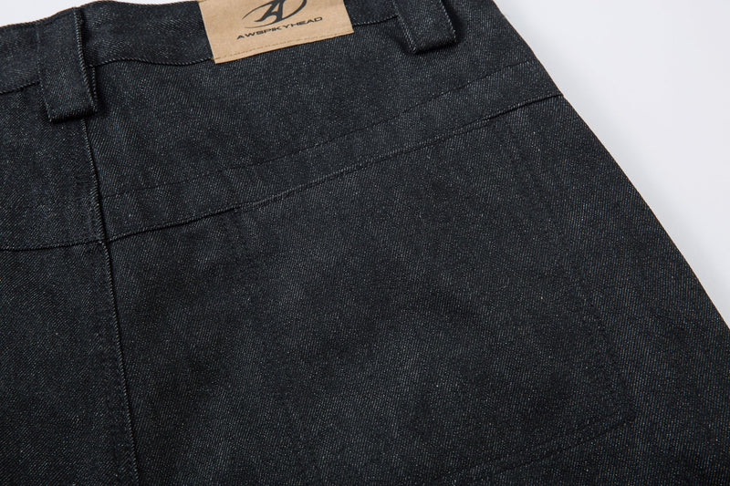 Close-up of back waistband pleats on dark denim pants with tan logo patch