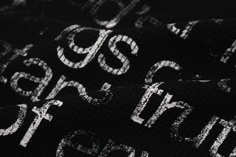 Close-up of black oversized tee fabric with distressed white gothic cross and script print