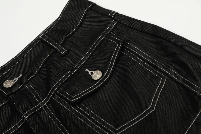 Close-up of the back pocket area on black denim pants with contrast stitching and metal buttons