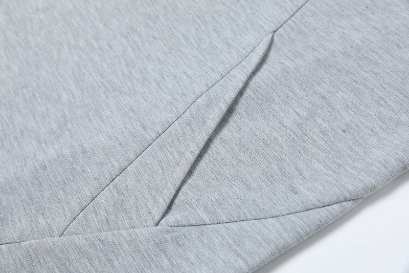Close-up of light gray oversized tee fabric with sharp geometric seam detailing and a structured minimalist cut