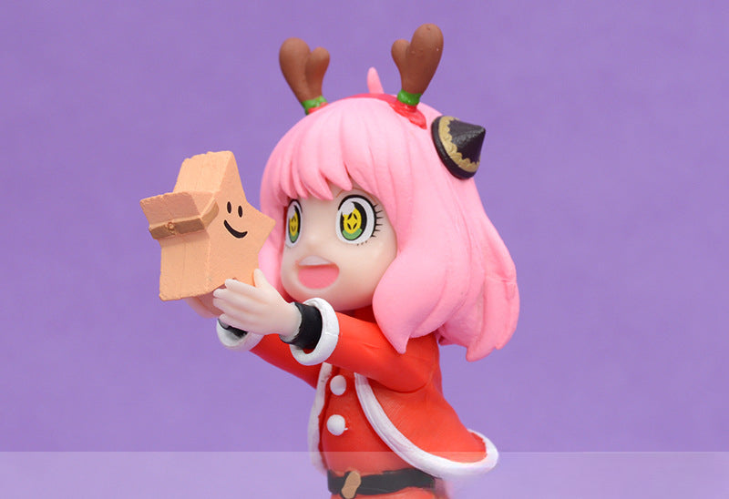 The Anya Forger Christmas PVC Figure - 18cm Holiday Edition by Spy × Family showcases a charming figurine of Anya Forger with pink hair, reindeer antlers, and a festive red outfit with white trim, holding a small box with a smile against a vibrant purple background—a perfect holiday-themed anime collectible.