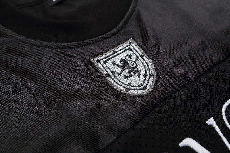 Close-up of black varsity football jersey T-shirt with embroidered crest and perforated streetwear fabric