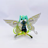 Standing against a white backdrop, the Racing Butterfly Hatsune Miku 12cm PVC Figure from Team MIKYO features mint green hair and metallic butterfly wings with "Onomot"-like circular designs. Dressed in a black outfit with vivid green accents, she&