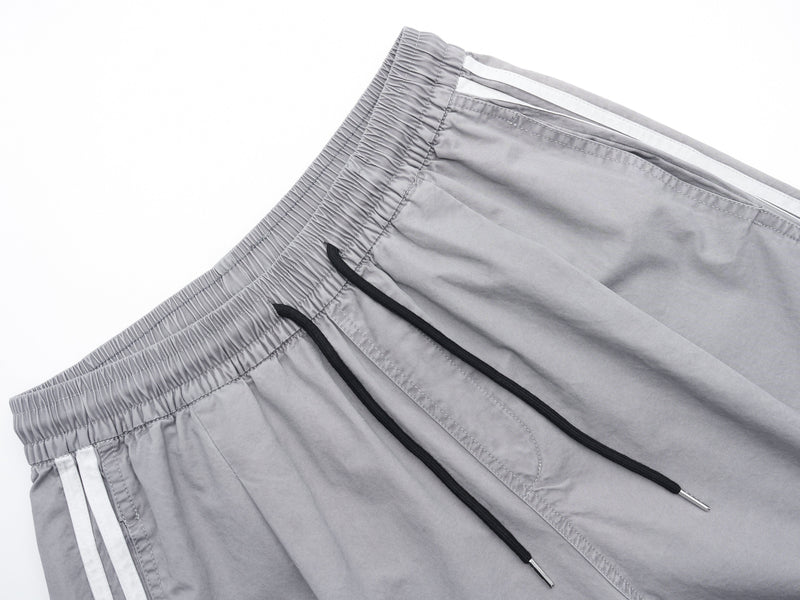 Close-up of gray shorts waistband with black drawstrings and side stripe detail