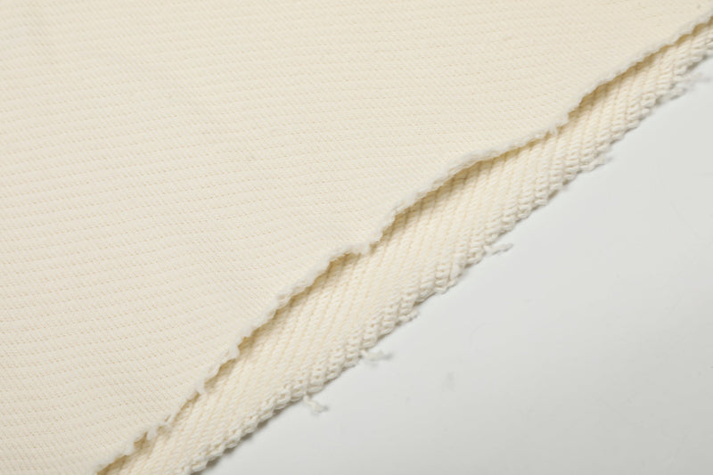 Close-up of cream sweatshirt hem with frayed edge and ribbed knit backing