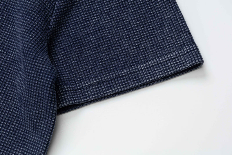 Close-up of a navy vintage washed polo tee sleeve with textured waffle knit fabric on a white background