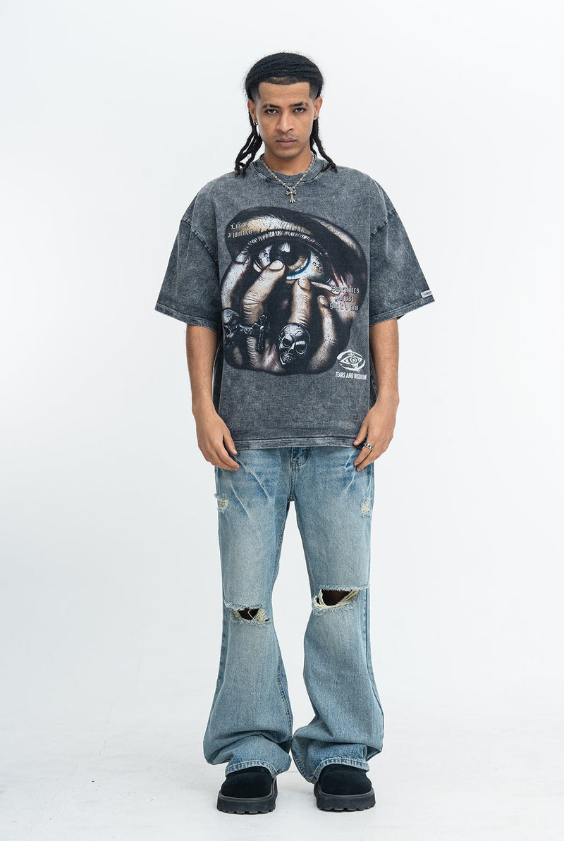 Oversized dark graphic tee with eye print, worn with distressed wide-leg jeans and black shoes