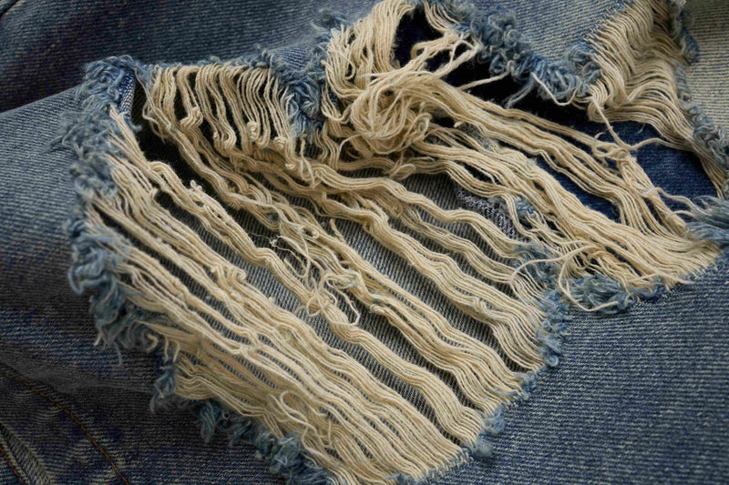 Close-up of frayed ripped patch on blue denim shorts leg