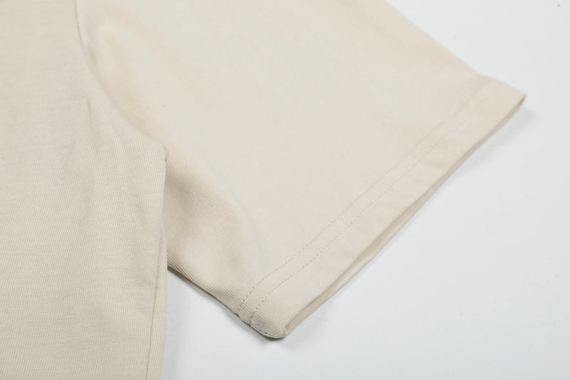 Close-up of a cream oversized cotton T-shirt sleeve with neat stitched hem and soft heavyweight fabric texture