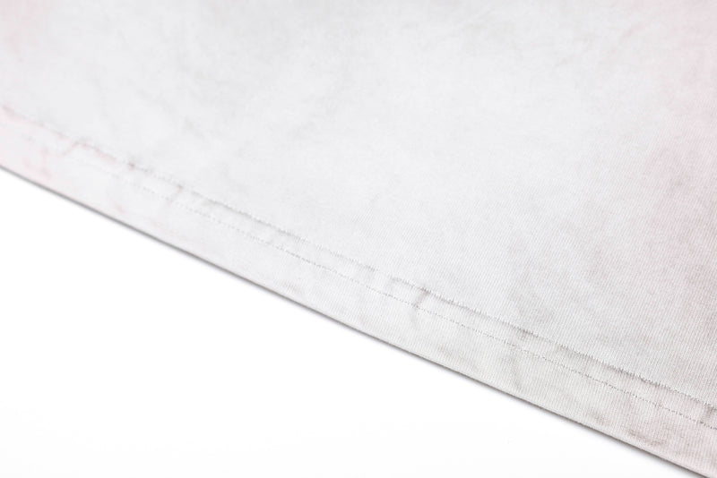 Close-up of a washed white vintage graphic tee hem with subtle stitch detailing and soft distressed fabric texture