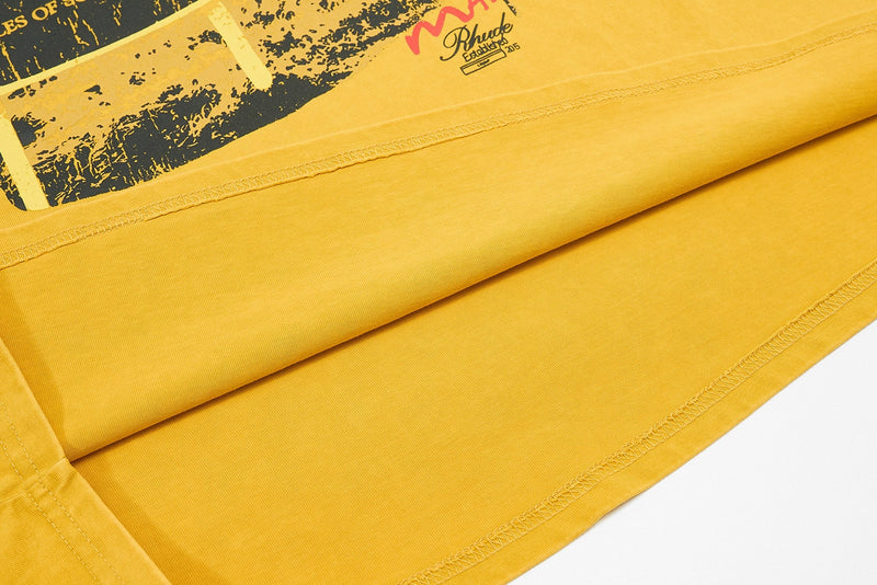Close-up of a yellow washed raglan tee with vintage graphic print and stitched hems, showcasing coastal streetwear style