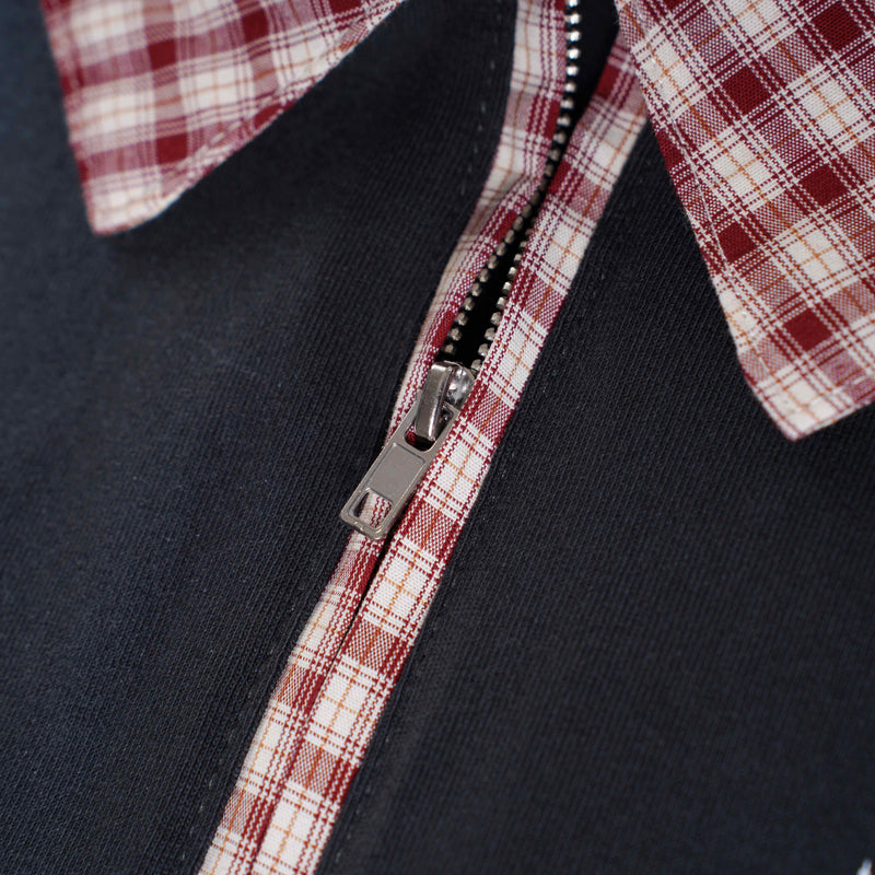 Close-up of a black polo with red plaid trim and a silver zipper on a textured fabric collar