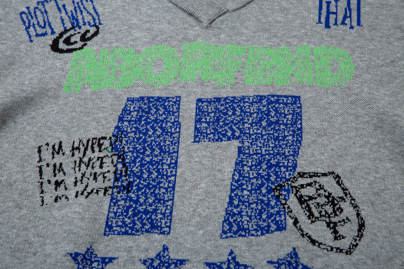 Front close-up of gray graphic knit sweater with green lettering, blue number print, and black doodle details