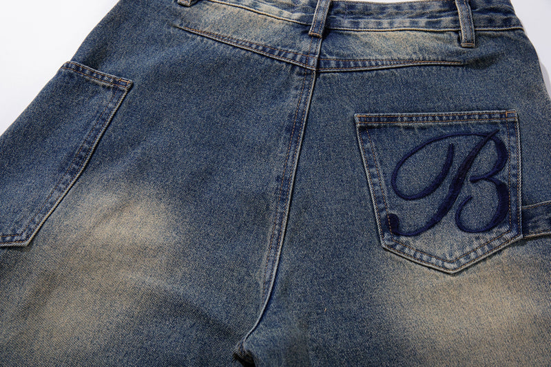 Close-up of back pocket with navy embroidered monogram on faded blue jeans
