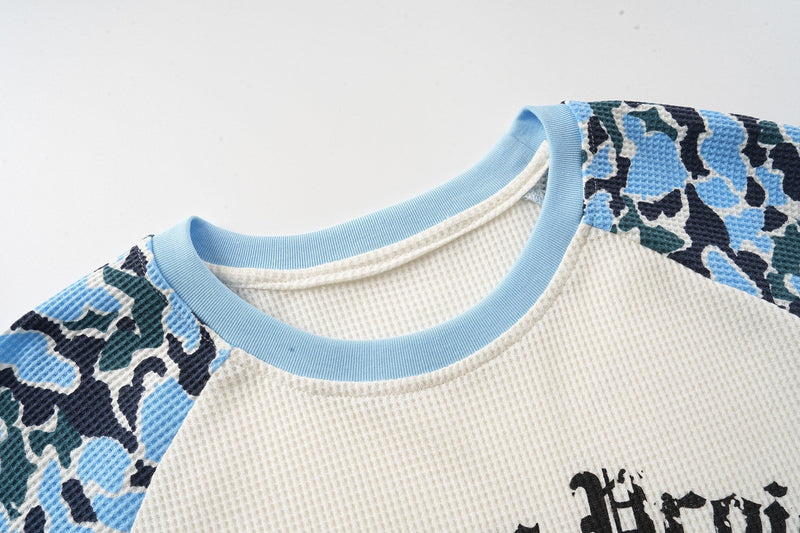 Close-up of light blue ribbed crew neck on cream waffle-knit tee with blue camo raglan shoulders