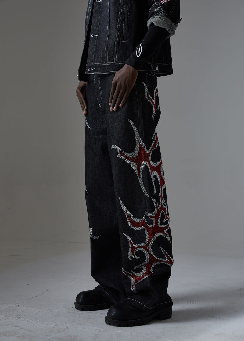 Side view of black wide-leg denim pants with a large red and silver rhinestone flame on the leg