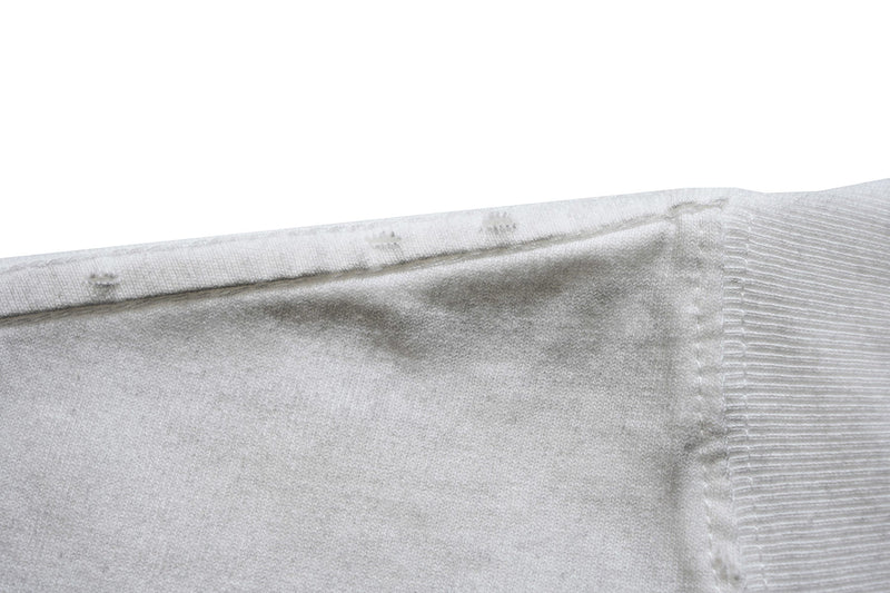Close-up of a white graphic T-shirt seam and ribbed cuff with soft fabric texture against a clean background
