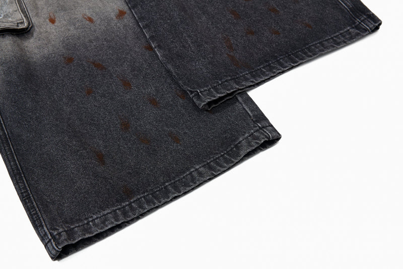 Close-up of the hem of dark gray wide-leg denim pants with brown paint speckles