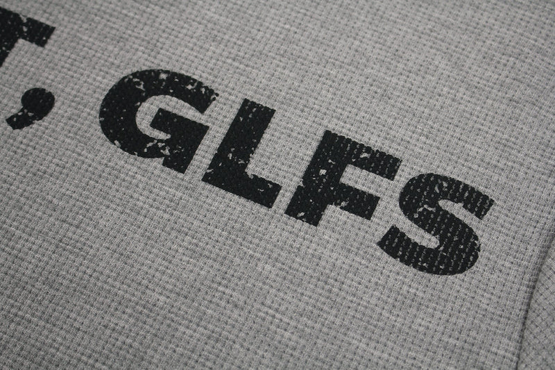 Close-up of a heather gray tee with distressed black gothic lettering spelling GLFS and textured knit fabric
