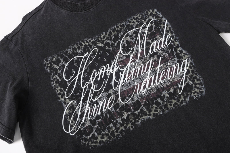 Close-up of black tee front graphic with camo print and white script lettering