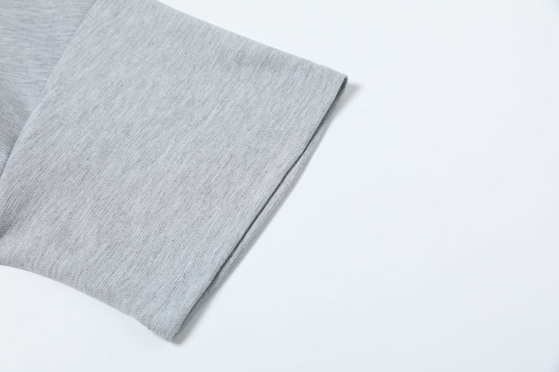 Close-up of a light gray oversized tee sleeve with structured hem and clean geometric seam details on a white background
