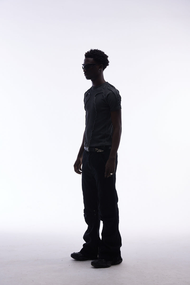 Model wearing a black raw seam compression tee, black pants, and sunglasses in a minimalist studio pose