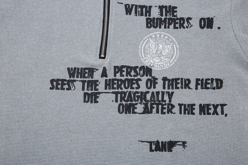 Gray half-zip graphic T-shirt with distressed black text and circular streetwear emblem on textured fabric