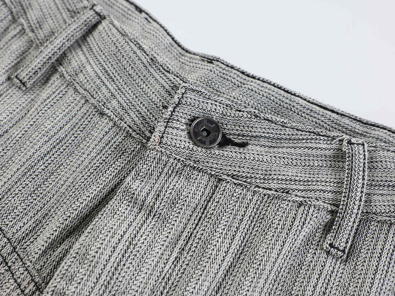 Close-up of front waistband button and seam detail on gray textured pants