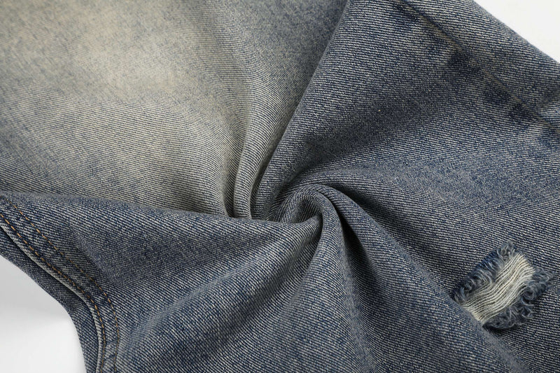 Close-up of denim fabric texture with faded wash and distressed rip detail