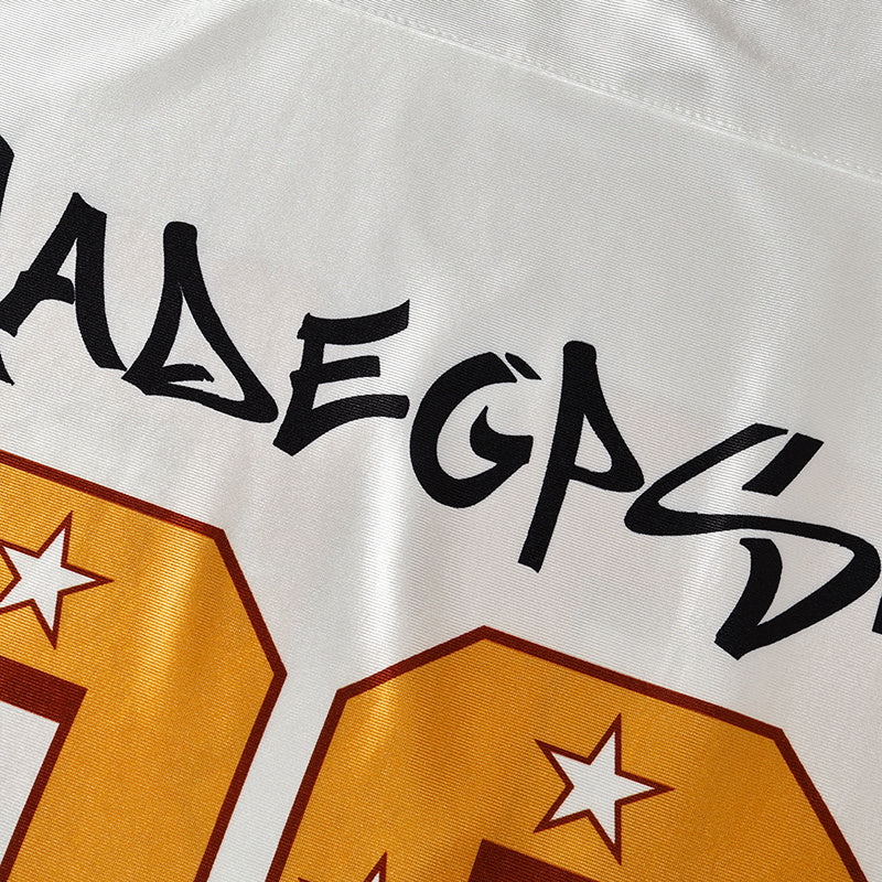 Close-up of a white football jersey with black graffiti-style lettering and bold gold number details with star accents