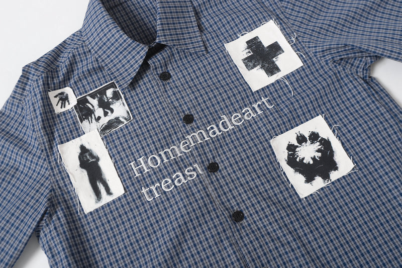 Front upper view of blue plaid overshirt with black button placket and graphic patches