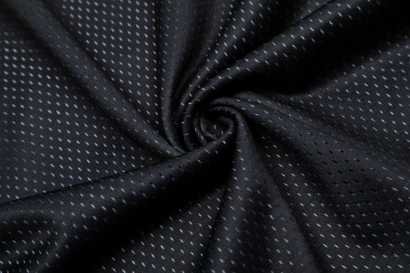 Close-up of black tech mesh jersey fabric with subtle white dotted pattern and textured oversized streetwear look