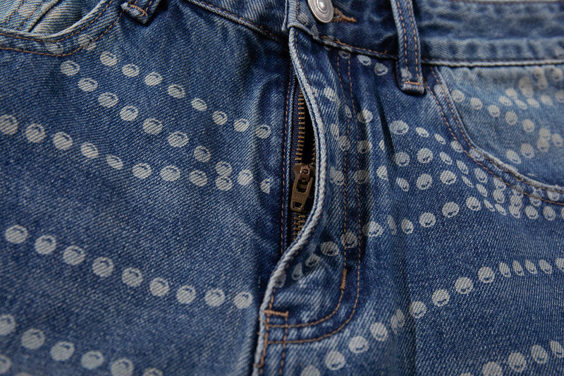 Close-up of front zipper and button on blue dot-pattern denim pants