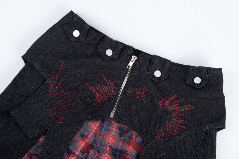 Close-up of black waistband with red stitched accents, zipper, and red plaid panel below