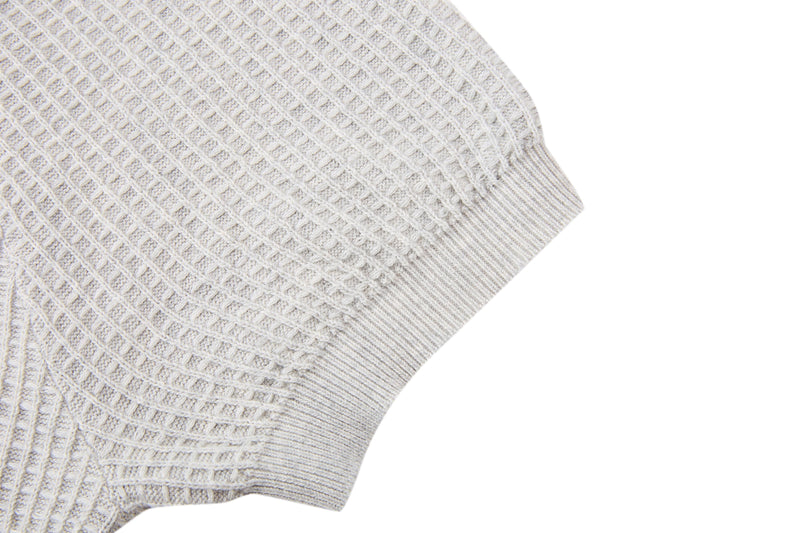 Close-up of a cream waffle knit short-sleeve sweater with ribbed hem and textured cotton blend fabric