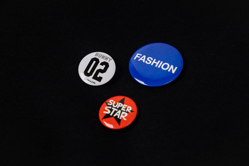 Close-up of three round badge accents on black hoodie, including blue, white, and red designs
