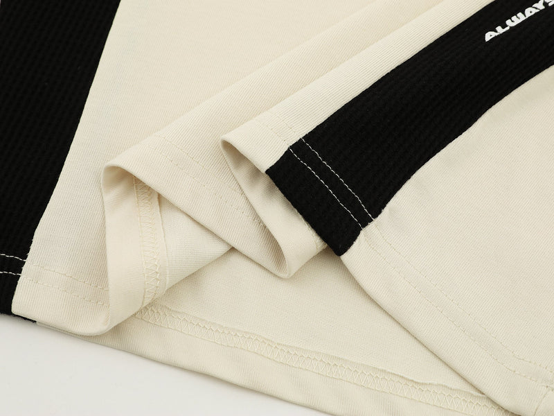 Close-up of folded cream and black athletic tee sleeves with contrast stitching and ribbed fabric texture