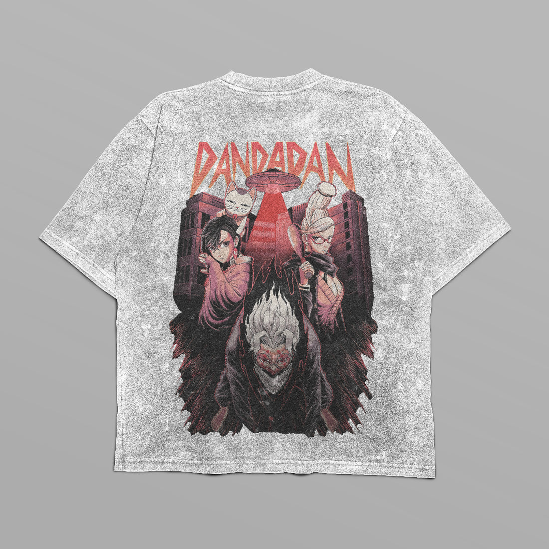 The Dandadan Oversized T-Shirt features a front logo and a back design with three anime characters under the stylized &quot;DANDADAN&quot; text. The urban backdrop has a reddish tint. Part of our streetwear line, it&