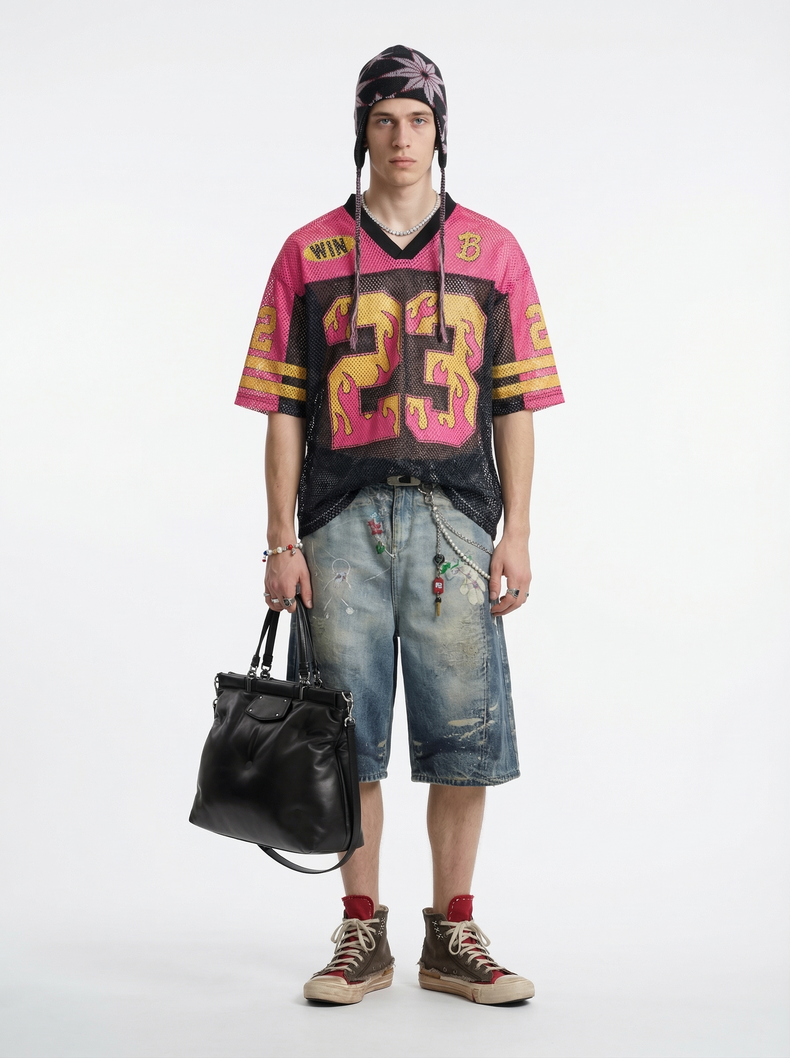 Model wearing a pink and black mesh football jersey with flame number 23, distressed denim shorts, and a black tote bag