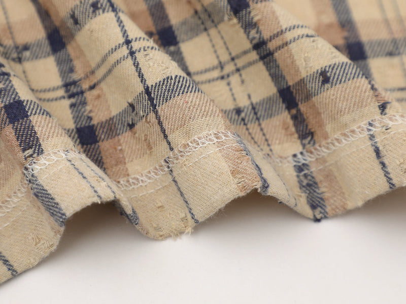 Close-up of beige and navy plaid shirt fabric with distressed edges and frayed seams, showcasing a streetwear look